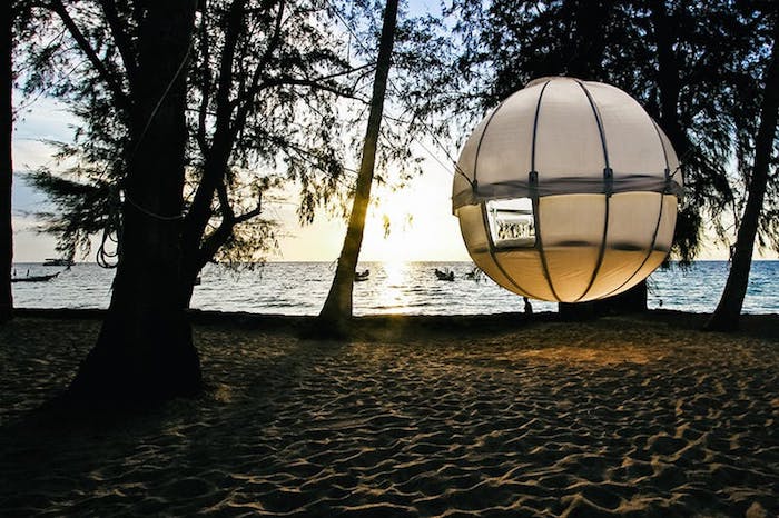 beach treehouse, round white orb, hanging above the ground, suspended from several trees, growing on a sandy shore, near the sea