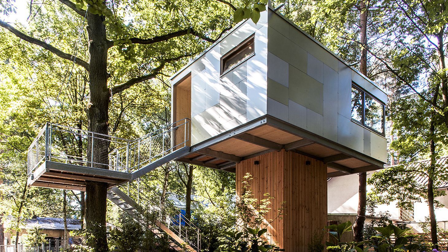 tile-covered industrial-style treehouse, suspended on a wooden platform, two windows and a door, accessible through a staircase, built around a nearby tree