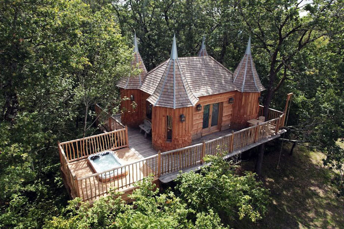 four tower-like wooden structures, attached to a castle-like tree house, built on a wooden platform, suspended over the ground, jacuzzi and a fence