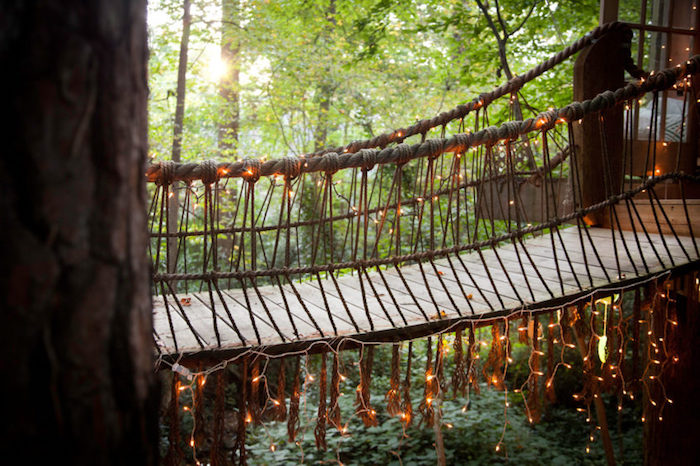 close up of a bridge, made from wooden planks and rope, treehouse designs, decorated with fairy lights, connecting two tree houses