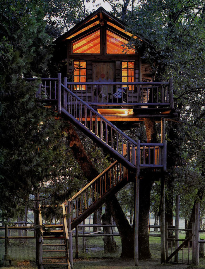 high above the ground, a tree house with several windows, illuminated from lamps inside, accessible through three sets of stairs