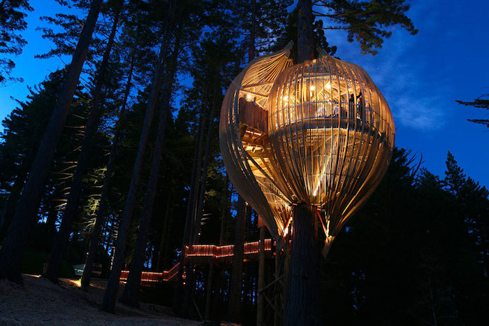 hot air balloon-shaped adult treehouse, made from wood and glass, and illuminated from within, with long staircase, dark nighttime forest