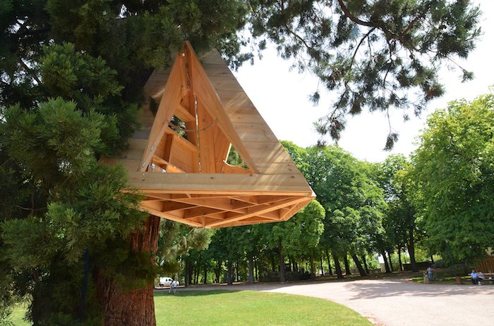 shelter made from pale wooden material, shaped like a pyramid, diy treehouse, hanging from a large fir tree, in a park