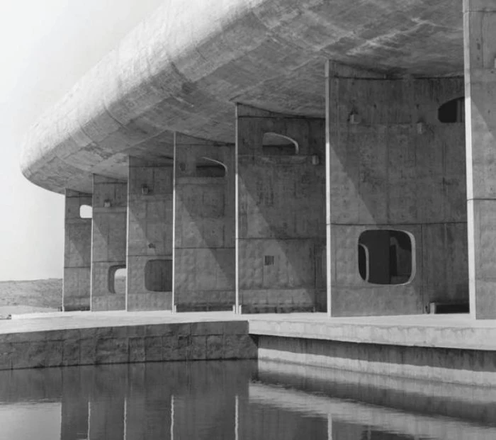 assembly building in chandigarh india, designed by le corbusier, oval concrete segment, propped up by several large concrete walls, featuring holes in different shapes 