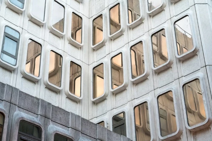 close up of a building, made of grey concrete, brutalism, featuring multiple rectangular windows, with rounded edges, covered in reflective glass
