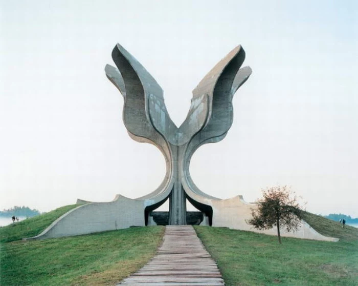wing-shaped concrete monument, in jasenovac croatia, built on a green hill, with a pathway and a small tree