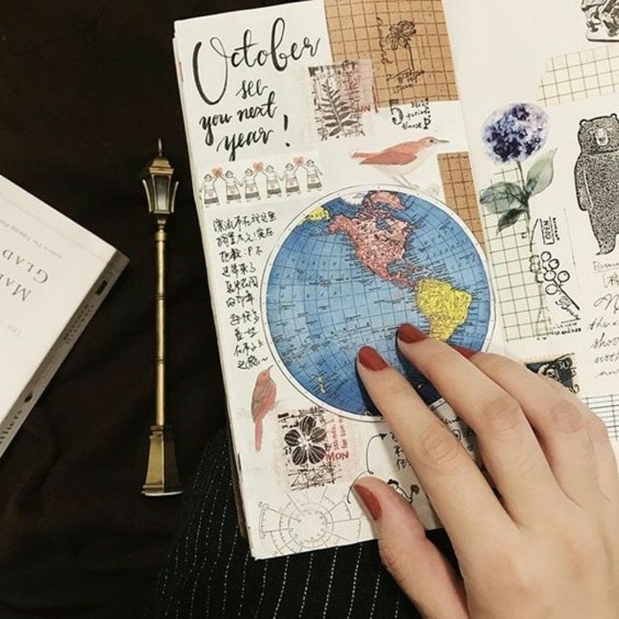 adventure journal, sketchbook with various cutouts, globe map, bear, birds, flowers, stamps, black writing, held by woman's had with red nail polish