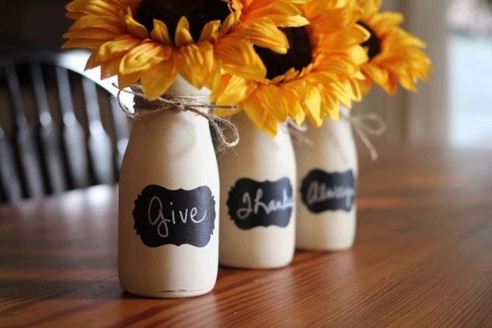  beautiful thanksgiving pictures, three bottles, painted white, with black labels reading give, thanks, always, tied with string, containing three sunflowers, placed on a wooden table with a chair in the background