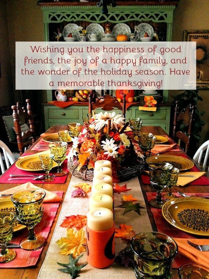 beautiful thanksgiving pictures, wooden table set up for thanksgiving, linen tablecloth, yellow decorated plates, green wine and water glasses, cutlery, white candles in orange candle holders, yellow, orange, red and green autumn leaves decorations, center piece containing flowers, yellow and orange napkins, white and brown chairs, green cabinet with crockery in the background, festive message 