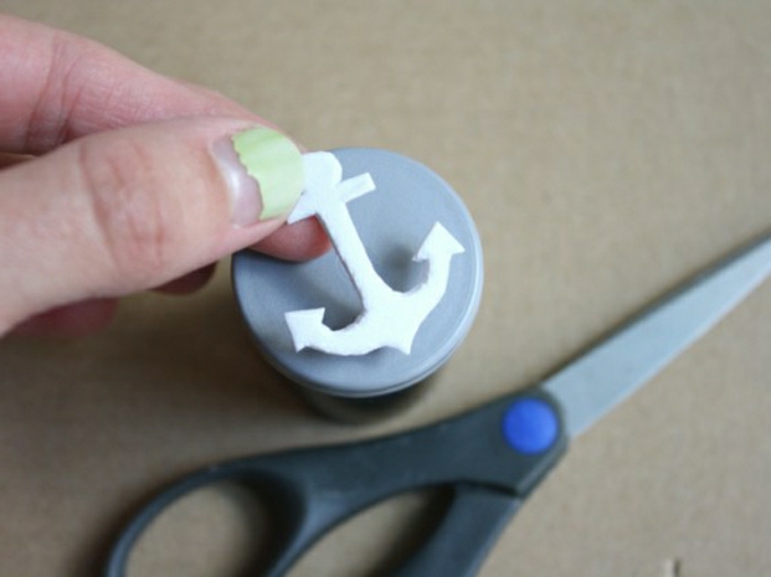 handmade gifts for dad, a woman's hand, with light green nail polish, holding an anchor shape from foam paper, dark blue scissors, light brown background