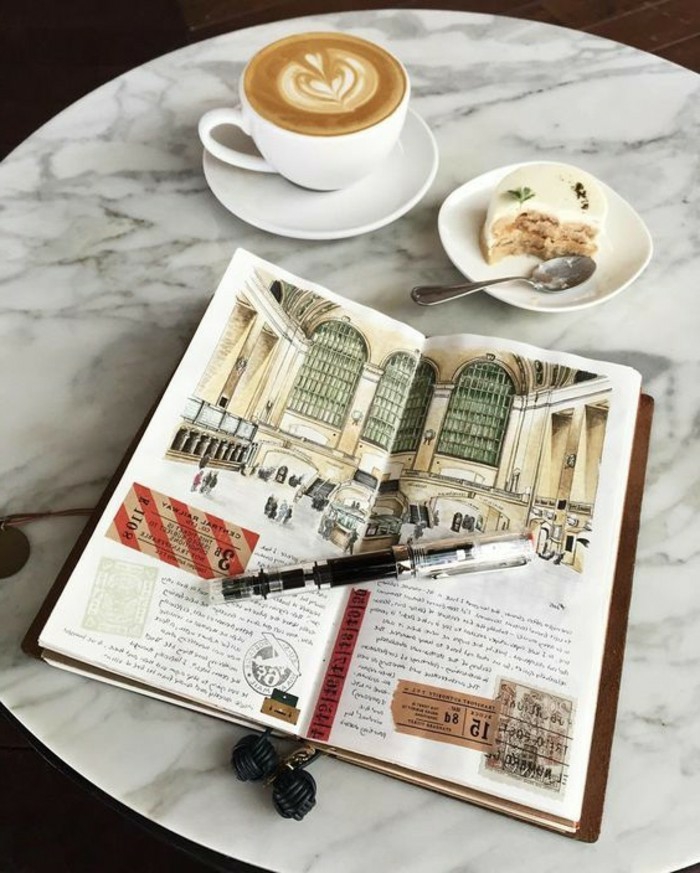 scrapbook layouts, sketchbook with colorful drawing, old travel tickets, white coffee cup with latte, a dessert, plates, pen, marble table