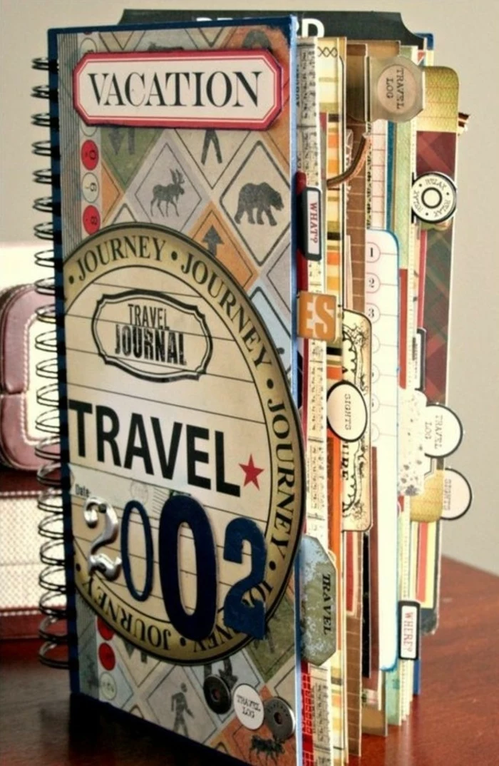 scrapbooking ideas, notebook with colorful pages and black binding, stickers, cutouts and a label saying vacation, on a wooden surface