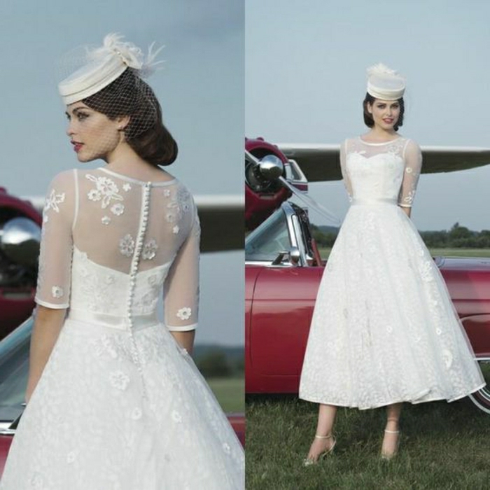 tea length wedding dresses, two images of a woman facing back and front, wearing a 1950s style tea length dress with lace and embroidery, small white cap with feather, standing in front of a retro car and a small plane 