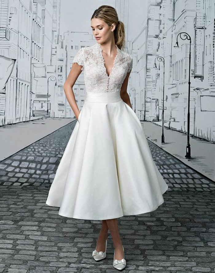 short lace wedding dress, blonde woman with hands in pockets looking down, wearing a white call-length wedding dress with lace and white shoes with bows, drawing of a city in background