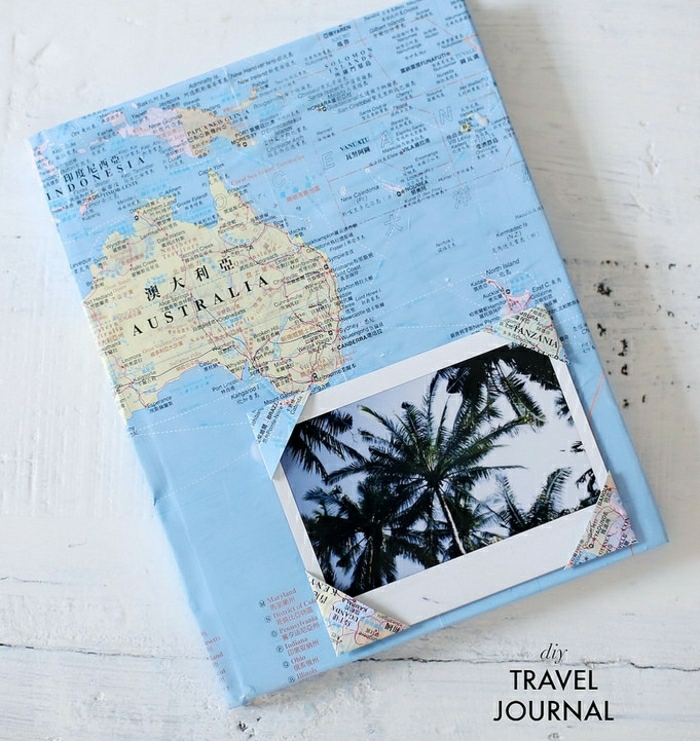  step dad gift ideas, hand decorated travel journal, made with a world map, on a white wooden table, with a palm tree photo stuck on the cover