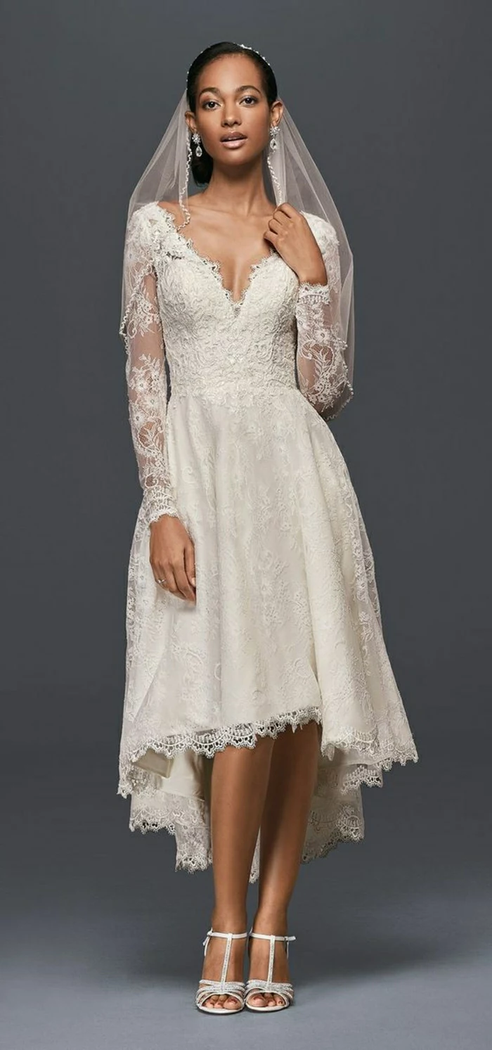 short lace wedding dress, african-american bride wearing a calf-length dress with lace and long sheer lace sleeves, with white sandals and a sheer veil on dark grey background