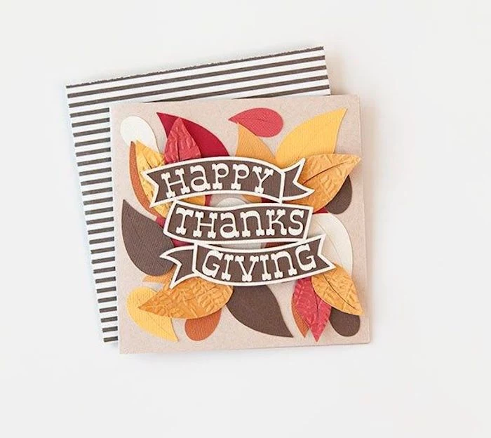 thanksgiving pictures, a festive card made with paper collage of differently colored leaf-shaped cutouts, with a brown banner reading happy thanksgiving, placed over a white and brown striped paper, on a white background