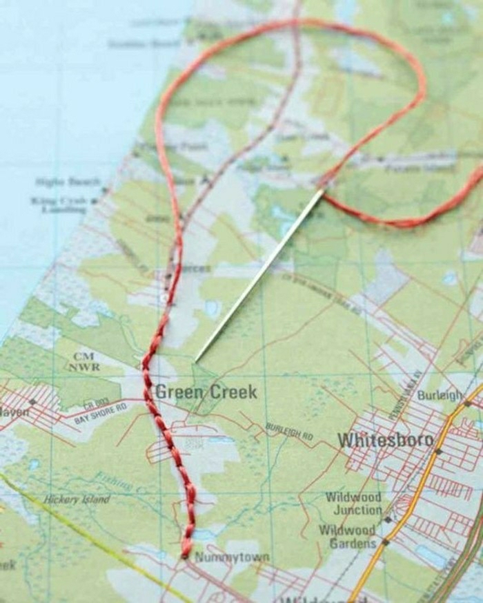 travel journal, close-up of map in light blue and green, with red thread stitched on it, silver needle