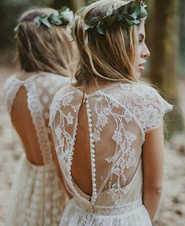 unique wedding dresses, blonde bride with green leaf-crown facing sideways, in a white lace dress with unbuttoned sheer lace back, standing near a mirror
