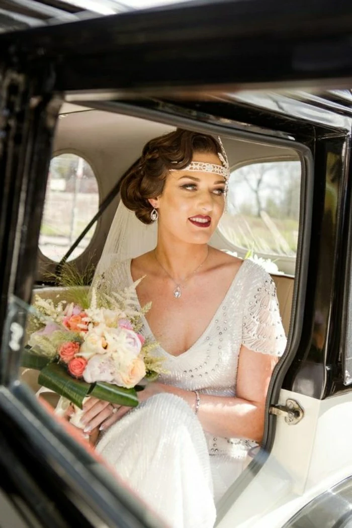 vintage inspired wedding dresses, bride with 1920s clothes hair and headband sitting in old-fashioned car and holding flowers