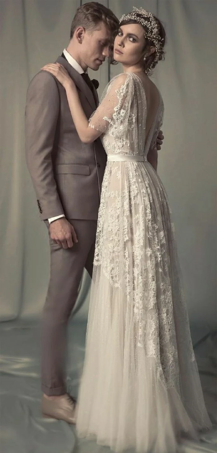 vintage inspired wedding dresses, bride in long vintage embroidered gown with lace and wearing a hair ornament hugging a man in a light brown suit
