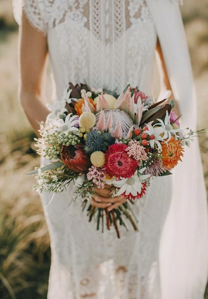 close-up of a bride in a lacy partly sheer dress, holding a bouquet with many different desert flowers in various colors