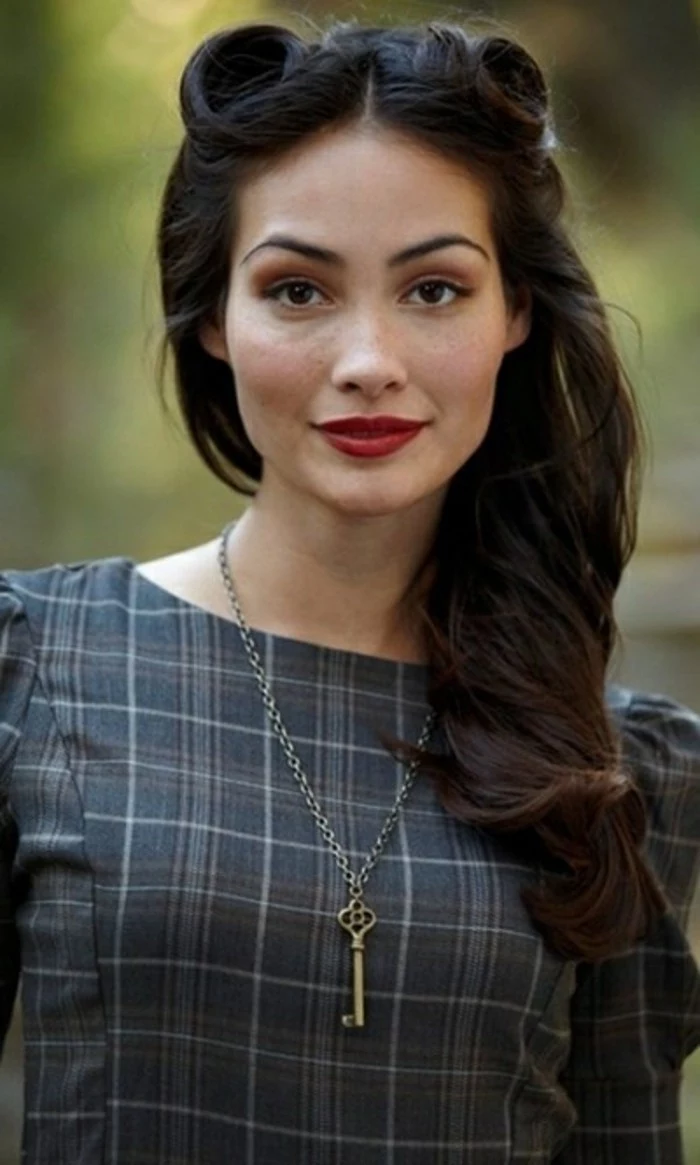 pinned up hairstyles for long hair, woman with victory rolls and long wavy dark hair, black eyes red lipstick and brown eye shadow with fake eyelashes and mascara, tartan top with ruffles and a key pendant