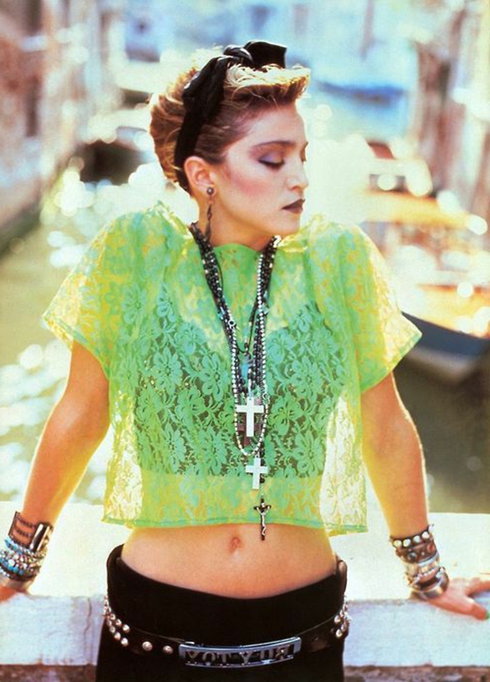 young madonna wearing heavy 80s make up, with short blonde hair and black hairband, wearing a sheer neon green lace top with black bra, black trousers a belt and various necklaces and bangles