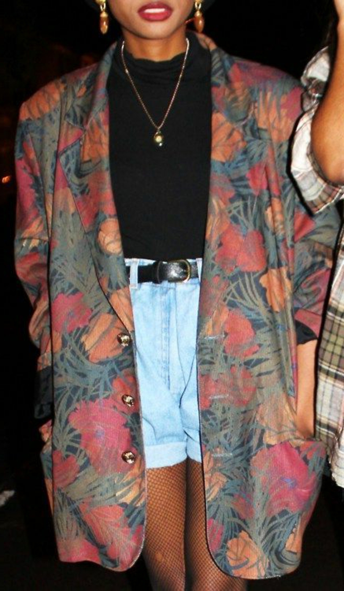 throwback thursday outfits, African-american woman wearing an over-sized tropical print blazer, black top and high-waisted light blue jean shorts, belt earrings and necklace, hands in pockets