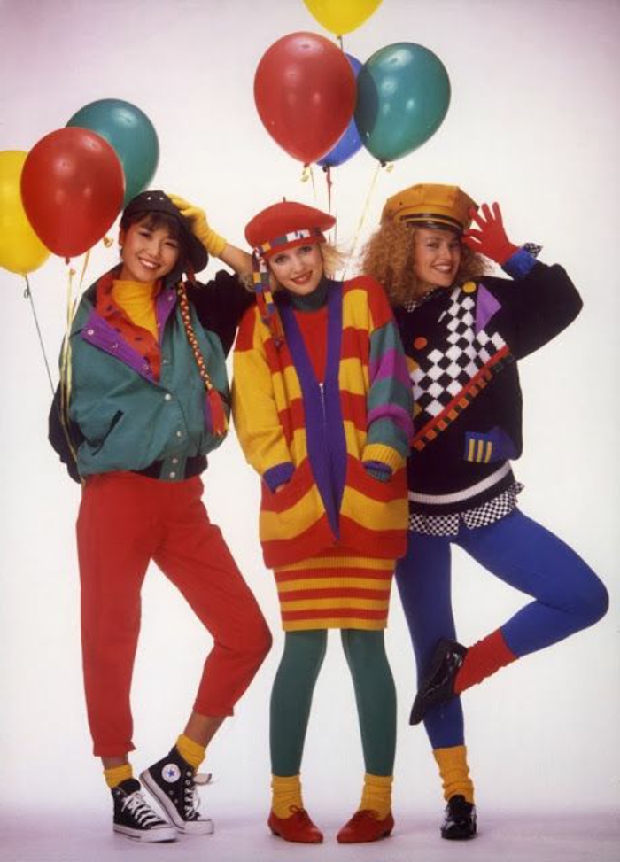 throwback outfits, three smiling young women in bright clothes, red pants green and blue leggings, yellow and red striped cardigan, green jacket yellow socks and colorful balloons 