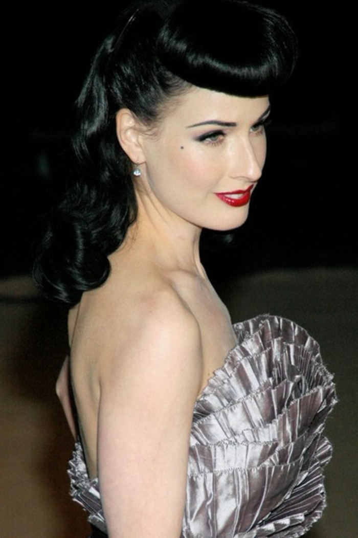 pinned up hairstyles for long hair, dita von teese, black hair with bettie bangs, red lipstick and white teeth, mascara eyeliner and a beauty spot, nude shoulders and a shiny dress with ruffles