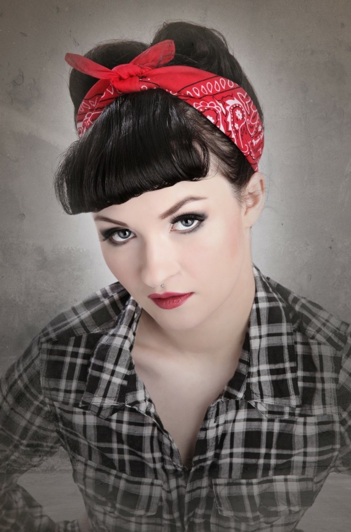 bettie bangs, woman seen from above, with black hair and curled bangs, wearing red bandanna with white and black details, red lipstick mascara and eyeliner, black and white plaid shirt