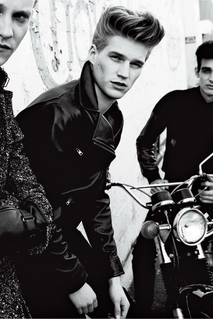 black and white photo of three young men, grey jacket and folded arms, black leather jacket and gelled up retro hair, motorcycle and dark hair