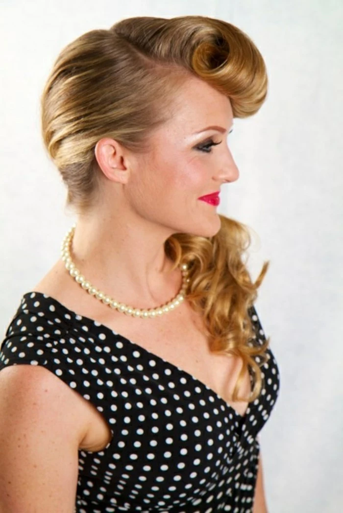 bettie bangs, blonde woman with curled bangs and long hair in ponytail, red lipstick and heavy eye make up, pearl necklace and black top with white polka dots