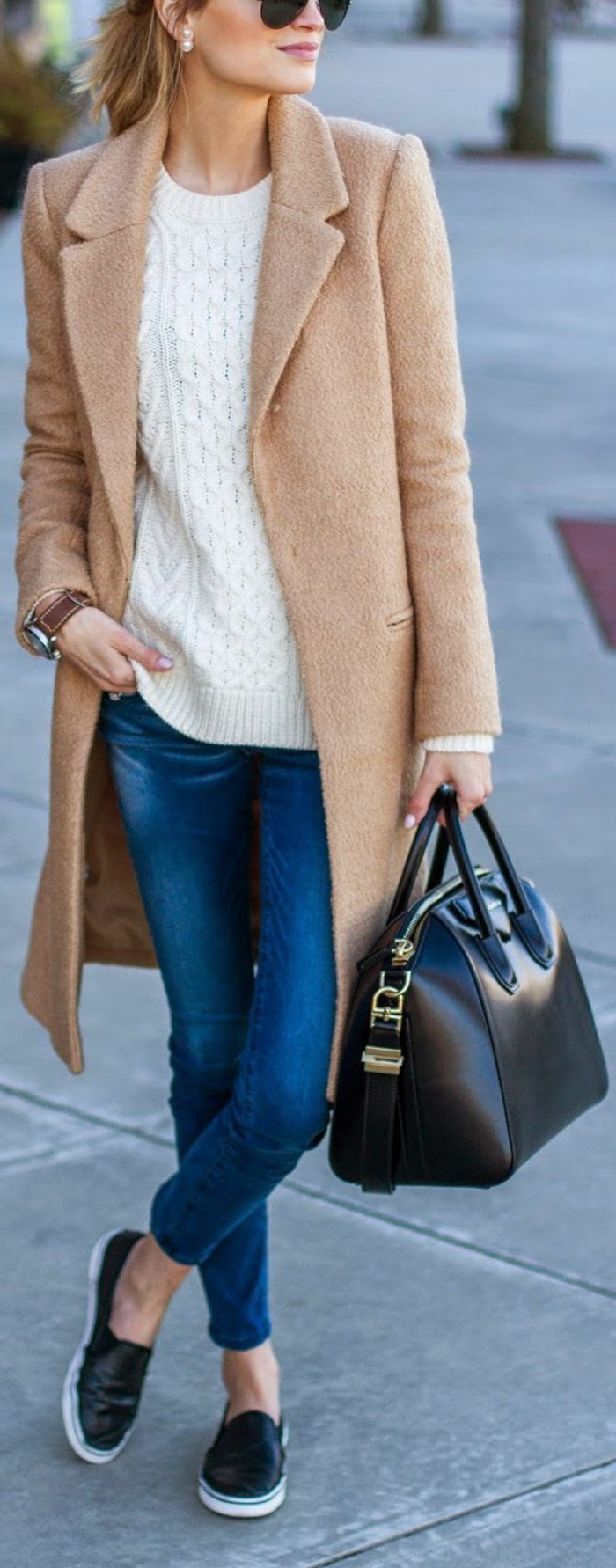 long camel brown coat over white sweater, blue jeans and black leather slip-on shoes, worn by blonde woman with sunglasses, holding black leather bag