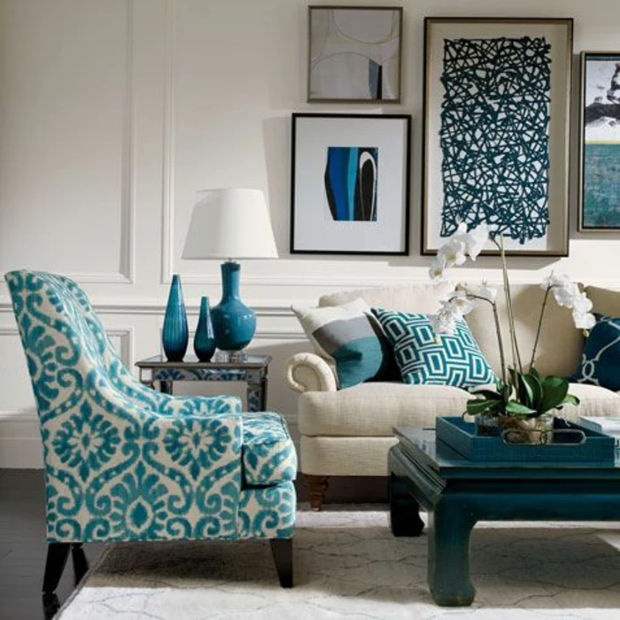 cream chair with blue pattern, black table and pale cream sofa with blue patterned cushions, white wall with plaster details, four framed images, blue lamp vases and trey white flower