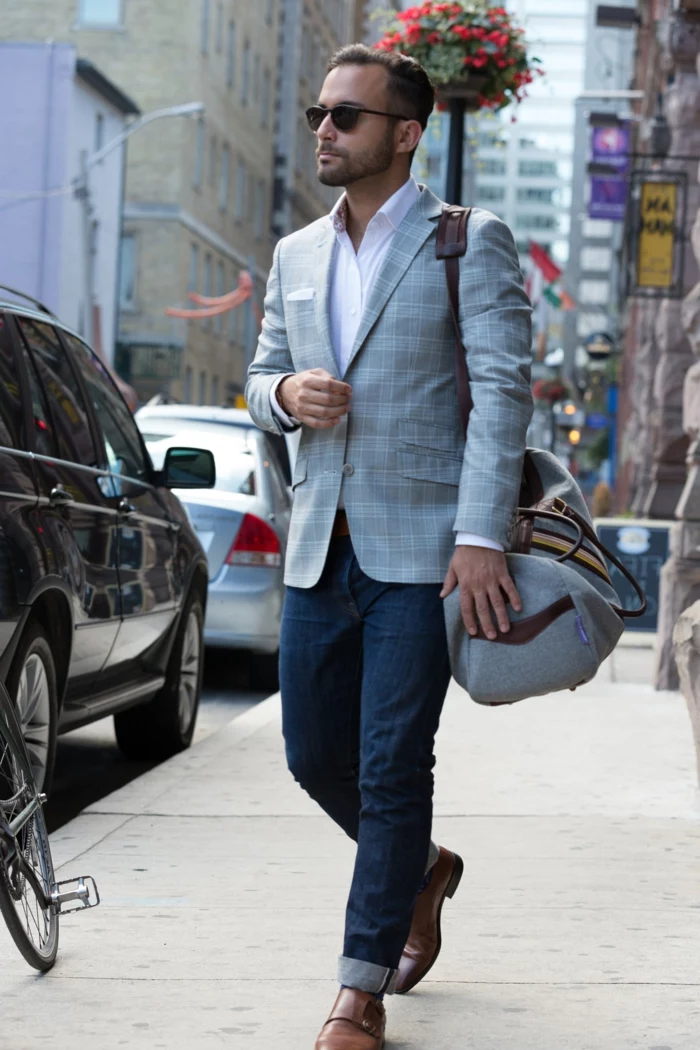 business professional attire, man with jeans and brown leather shoes, wearing light grey chequered blazer over pale pink shirt, with sunglasses and sports bag