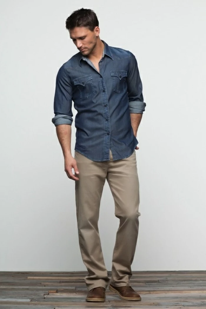 business casual outfits, man with short brown hair, looking down with hand in back pocket, pale khaki pants with denim shirt and brown shoes