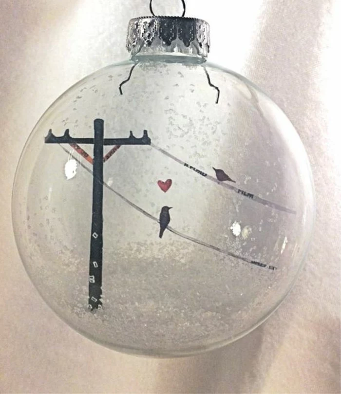 cheap christmas gift ideas, one clear glass bauble with silver cap, filled with fake snow, and a drawing of two birds perched on power lines with a red heart