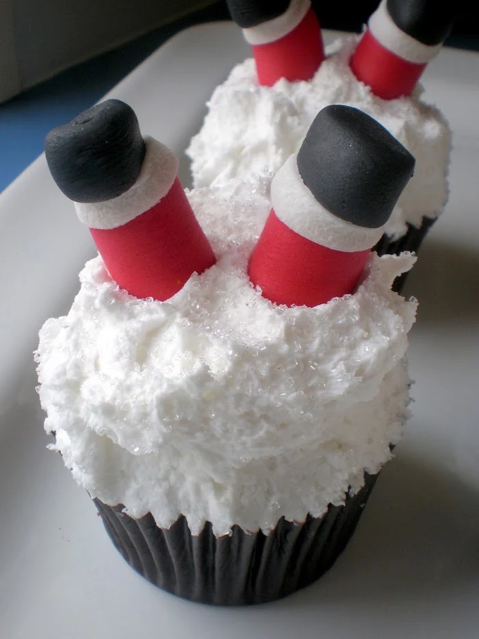 christmas baking ideas, two cupcakes with white sparkly snow-like frosting, decorated with santa's legs made from fondant