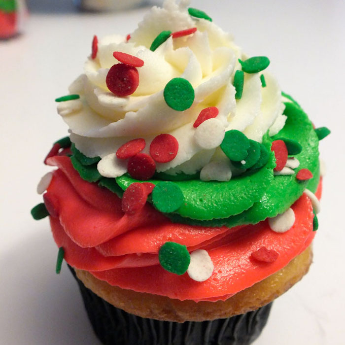 christmas baking ideas, light colored cupcake with black wrapper, with white green and red frosting, decorated with red white and green sprinkles