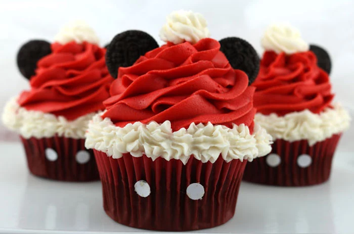christmas flavors, three cupcakes with dark red wrappers, with red and white frosting and two oreo biscuits each, made to look like mickey mouse with a santa hat