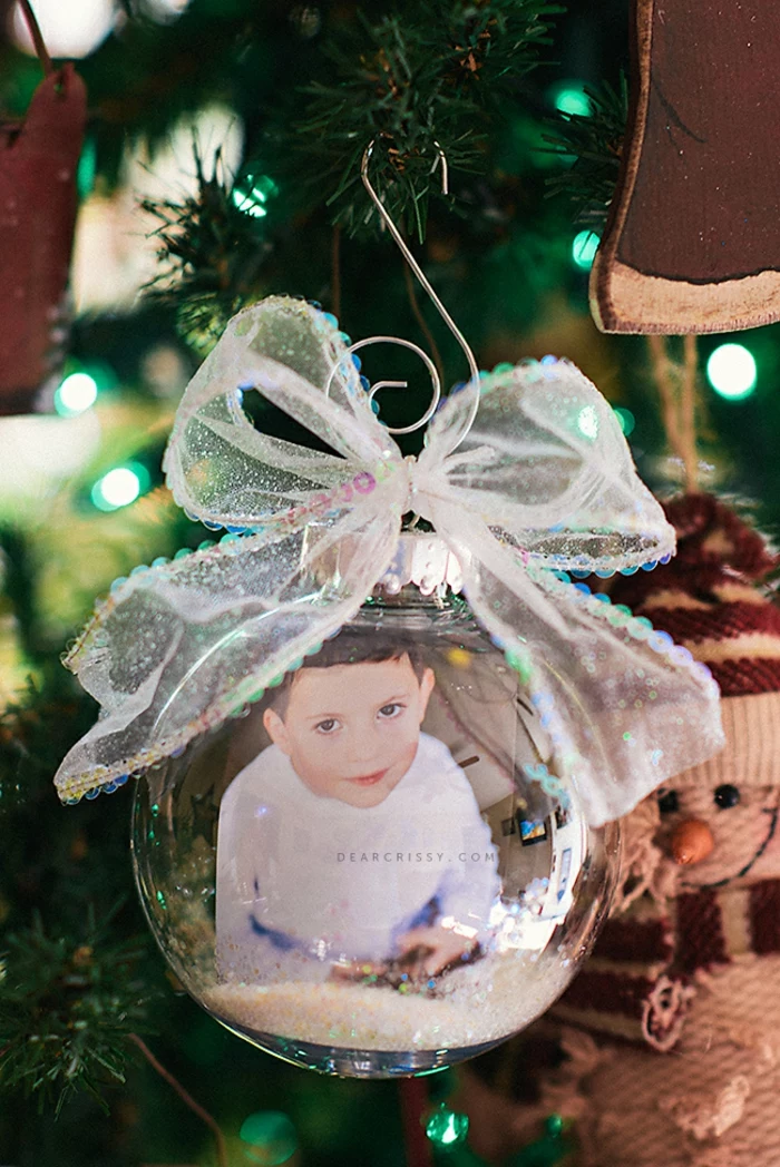 cheap christmas gift ideas, a photo of a small boy inside a clear glass christmas bauble with some glitter, tied with a sheer sparkling ribbon, attached to a tree with a metal hook