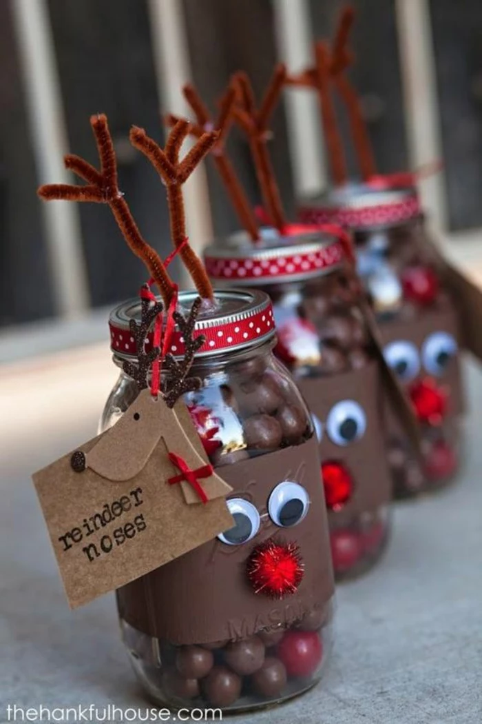 family christmas gifts, three mason jars decorated with a brown paper strip, with googly eyes and red a pom-pom nose, with wire antlers stuck on lids, red dotted ribbon and carboard label