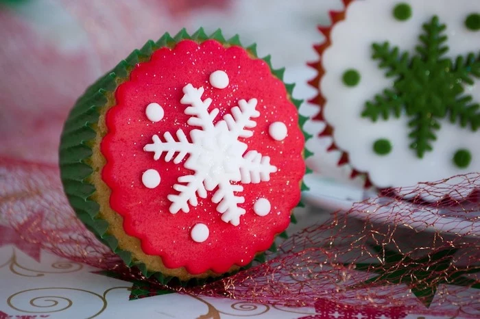 mini cupcake recipes, close up of cupcake in green wrapper, with red fondant icing and white snowflake, near cupcake with red wrapper and white icing with green snowflake