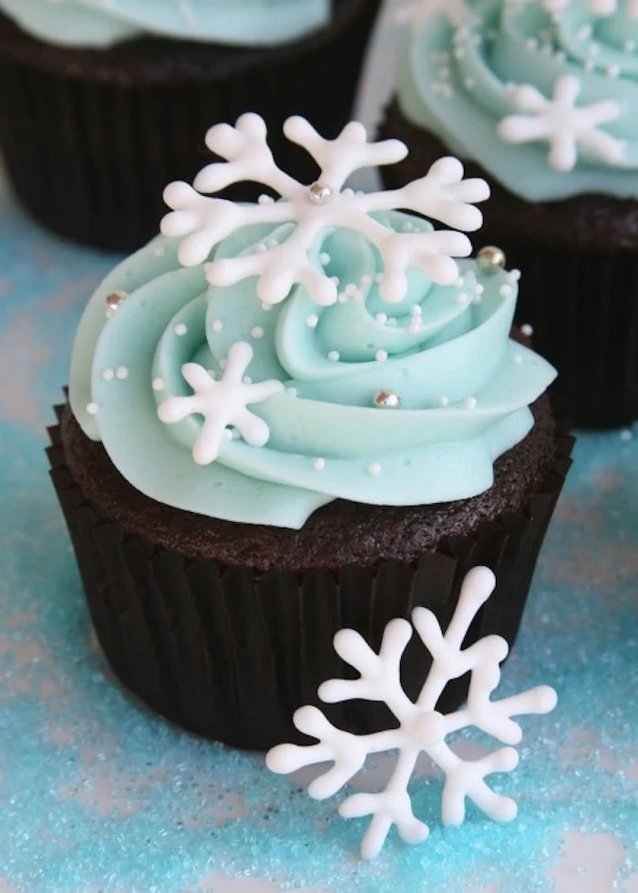 christmas flavors, chocolate cupcake with black wrapper, light blue frosting, decorated with snowflake shapes, white sprinkles and silver pearls 
