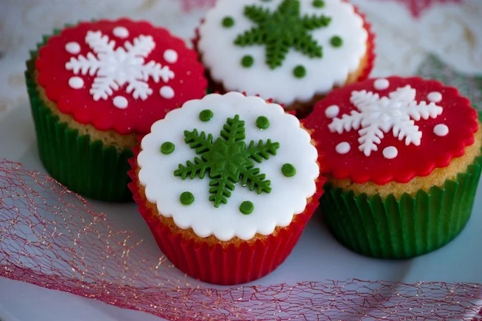mini cupcake recipes, four cupcakes with white red and green fondant icing, in red or green wrappers, decorated with green or white fondant snowflakes