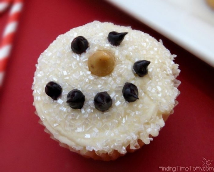 cupcake ideas, cupcake with white sparkly frosting, decorated with chocolate icing and caramel chip, made to look like a snow man, on red and white background