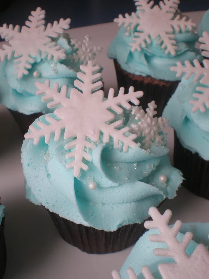 holiday cupcakes, several cupcakes with dark wrappers, light blue frosting, decorated with white snowflakes sprinkles and pearls