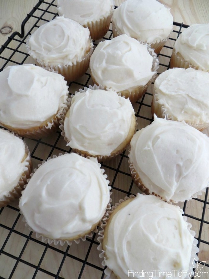 cupcake ideas, twelve light-colored cupcakes, with white creamy frosting, on black metal oven grate